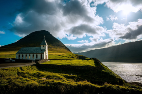 Church on a hillside next to a body of water on a cloudy day