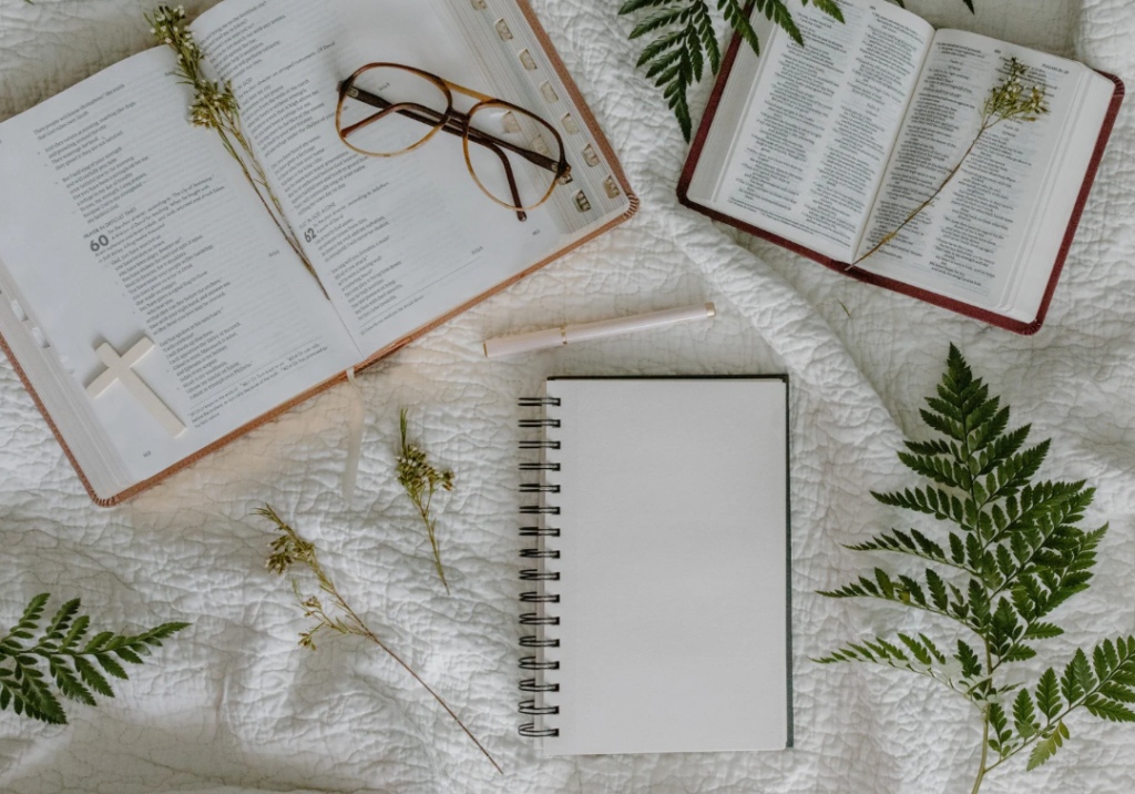 Two open Bibles, a pair of glasses, a pen, and a journal