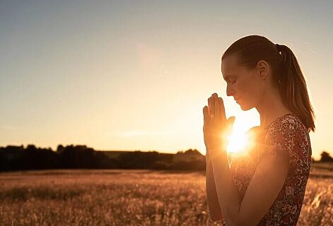 Woman praying to God as sun rises