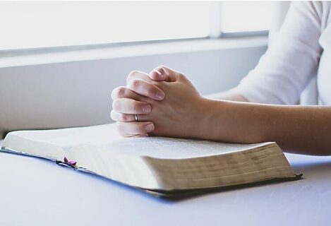 Woman’s hands folded in prayer on top of Bible
