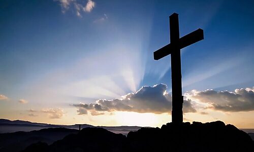 Cross on a hill with sunrise covered by clouds
