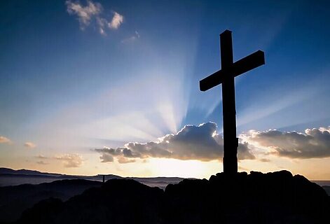 Cross on a hill with sunrise covered by clouds