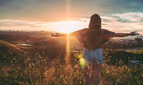 Woman with arms outstretched standing in field at sunrise