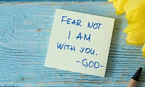 Tulips, pen, and sticky note saying “fear not I am with you God” on a table illustrate hearing God in season of chaos