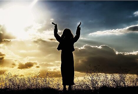 Woman with hands lifted to bright sky as if in prayer to illustrate God speaking in many different ways