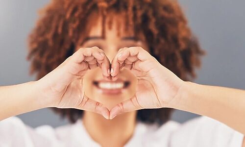 Woman smiling and forming heart with hands represents loving self because designed for God’s calling