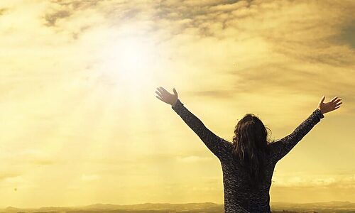 Woman raising hands to sun in sky illustrate discerning and hearing God’s voice