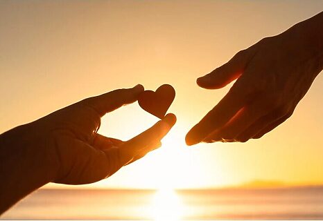 Two hands exchanging a heart with sunset in the background illustrate God using someone to be a blessing