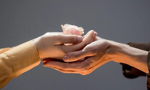 Person using two hands to support another woman’s hands. Other woman is holding a pink rose. Image illustrates serving God by helping others.