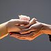 Person using two hands to support another woman’s hands. Other woman is holding a pink rose. Image illustrates serving God by helping others.