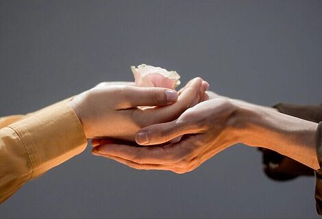 Person using two hands to support another woman’s hands. Other woman is holding a pink rose. Image illustrates serving God by helping others.