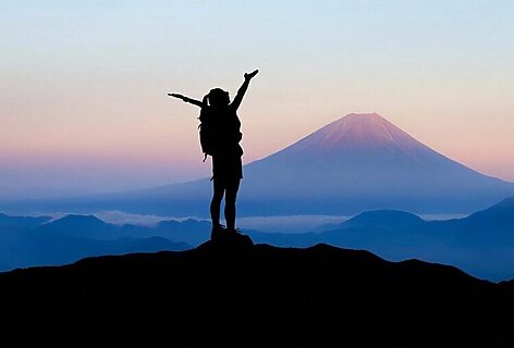 Woman on mountaintop with hands raised in triumph illustrate success when finding calling