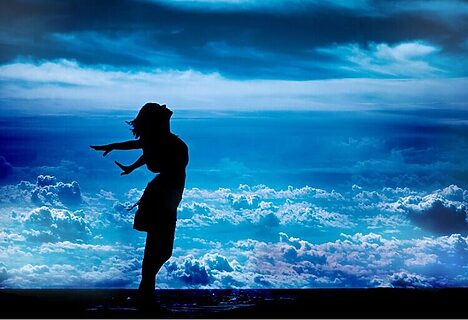 Woman with hands in air in front of cloudy sky represent surrendering to God’s calling