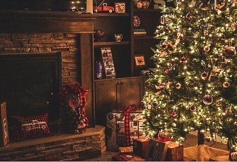 Lit Christmas tree with presents underneath and fireplace beside it represent Christmas Eve