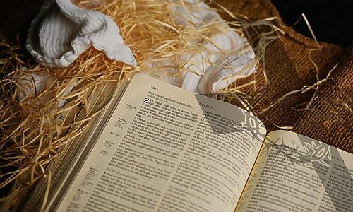 Open Bible, straw, blanket, and burlap with shadow of cross allude to true purpose of Christmas