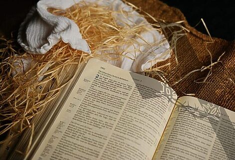 Open Bible, straw, blanket, and burlap with shadow of cross allude to true purpose of Christmas