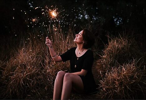 Woman sitting outside holding sparkler and smiling illustrates contentment
