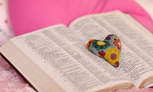 Image of Bible laying open and heart trinket sitting in the center illustrate God’s love through the Bible