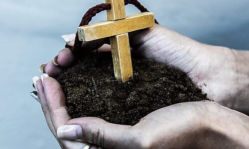Image of woman holding a cross in a patch of dirt illustrates growing faith in 2025