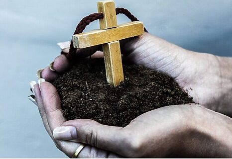 Image of woman holding a cross in a patch of dirt illustrates growing faith in 2025