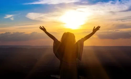 Woman enjoying sunrise with outstretched hands represent hope while waiting on God