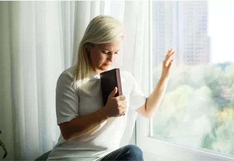 Image of women praying with Bible by window illustrates pursuing faith when feeling distant from God